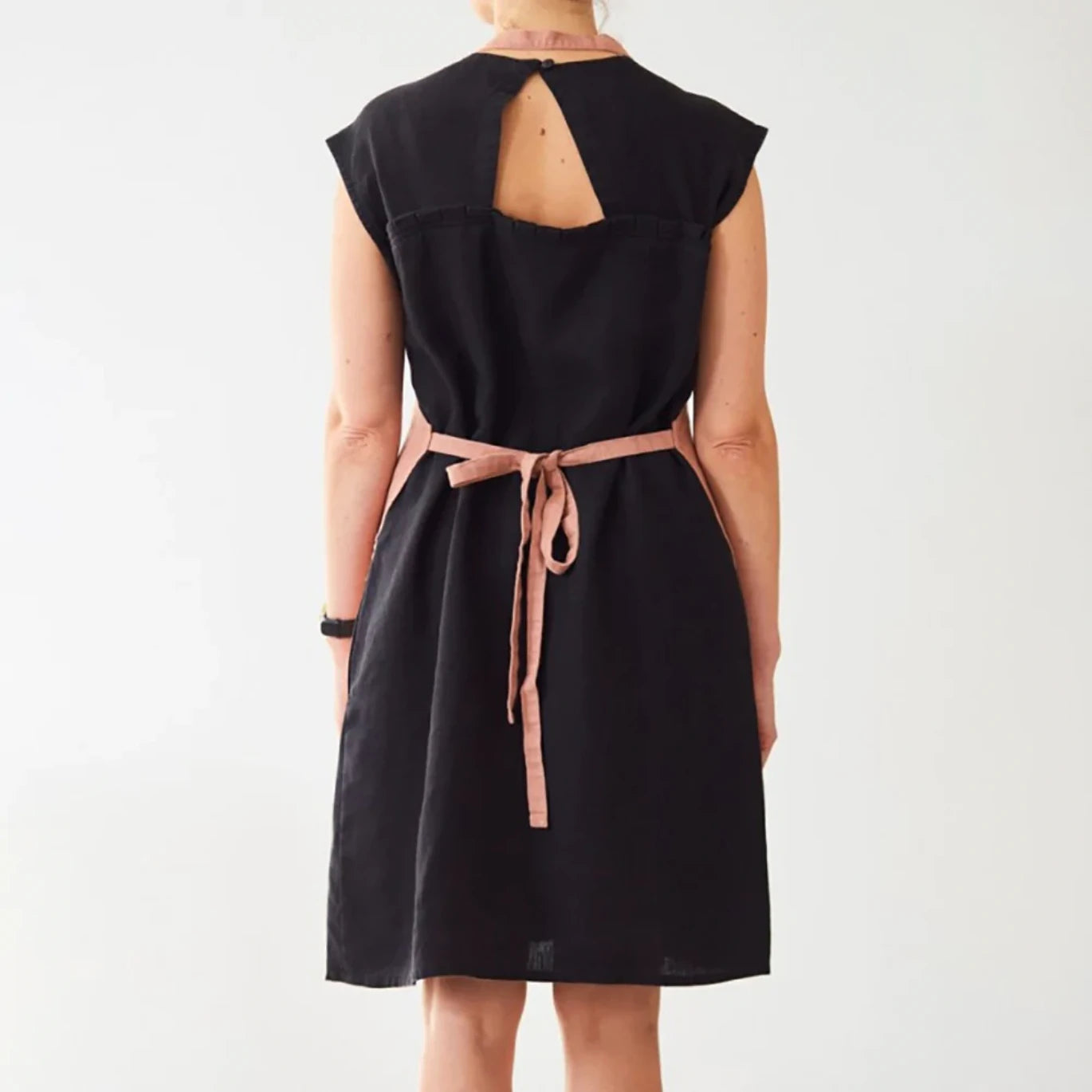 En person har knutit ett aprikosfärgat linneförkläde i ryggen.