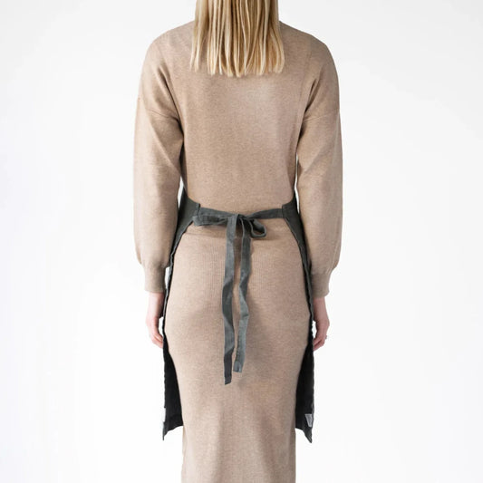 En kvinna bär ett grått köksförkläde i linne som har knutits i ryggen.