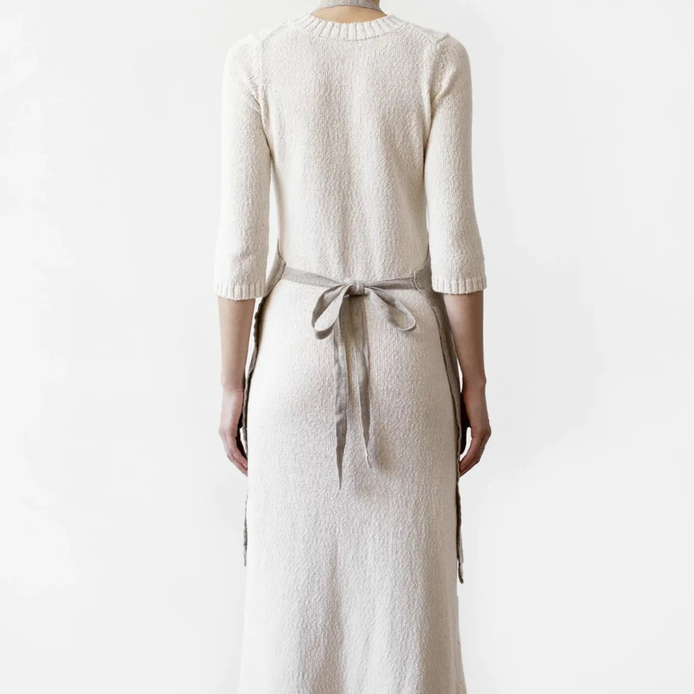 En kvinna bär ett köksförkläde i linne och har knutit det i ryggen.