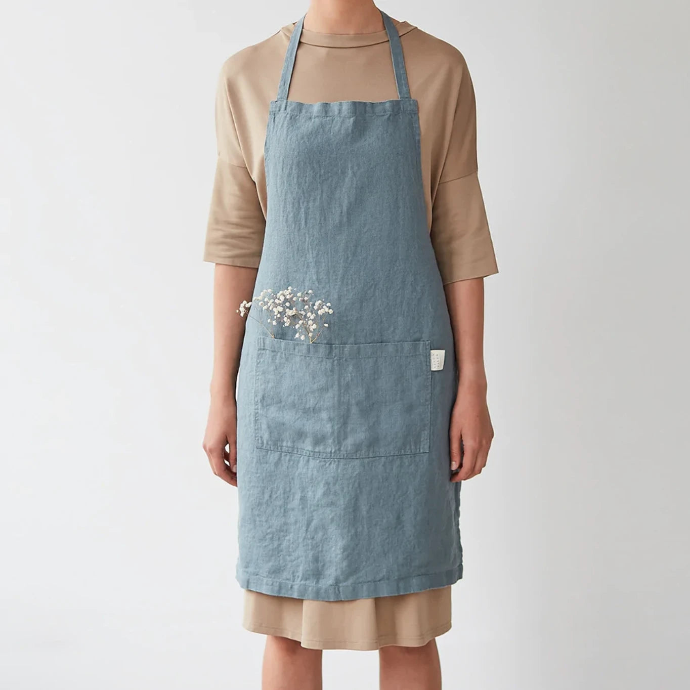 Ett blått köksförkläde i linne som har fickor framtill och har knutits i ryggen. 