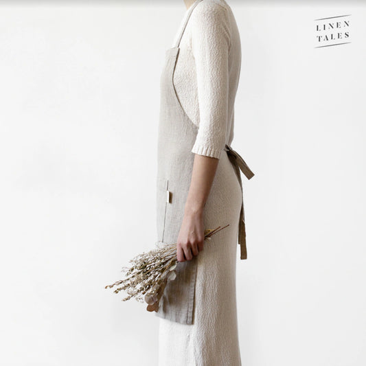 En kvinna bär ett naturellt linneförkläde över halsen och har knutit det i ryggen.