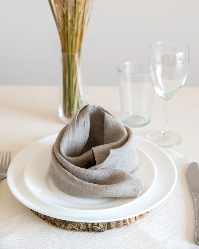En handsydd beige linneservett ligger på en tallrik.