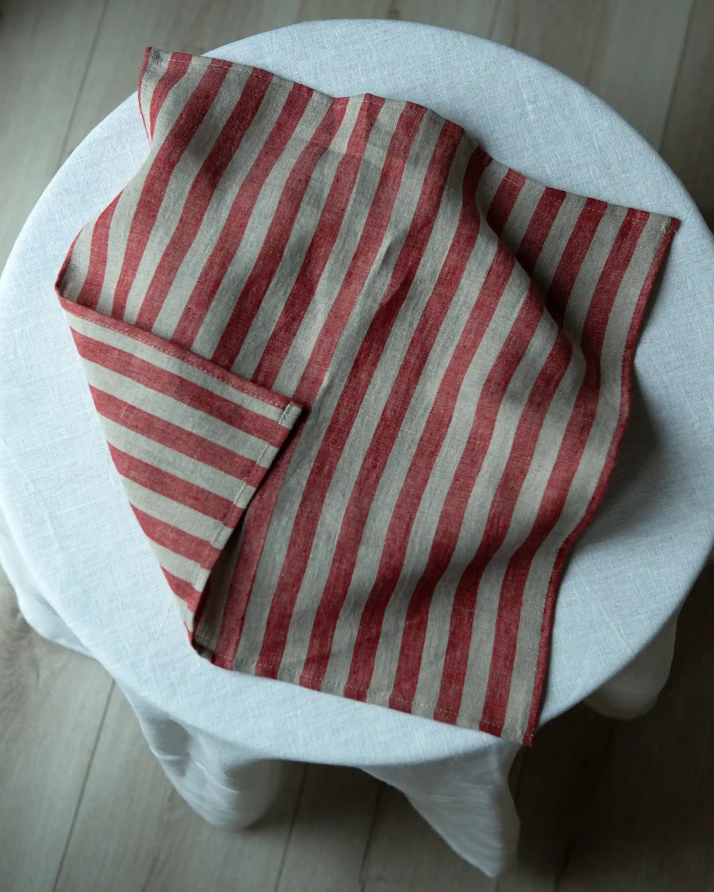 En handsydd linneservett med röda och beige ränder ligger på ett bord. 