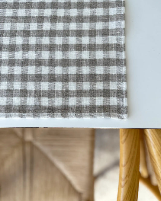 Ett handsytt bordsunderlägg i stentvättat rutigt linnetyg som ligger på ett vitt bord. 