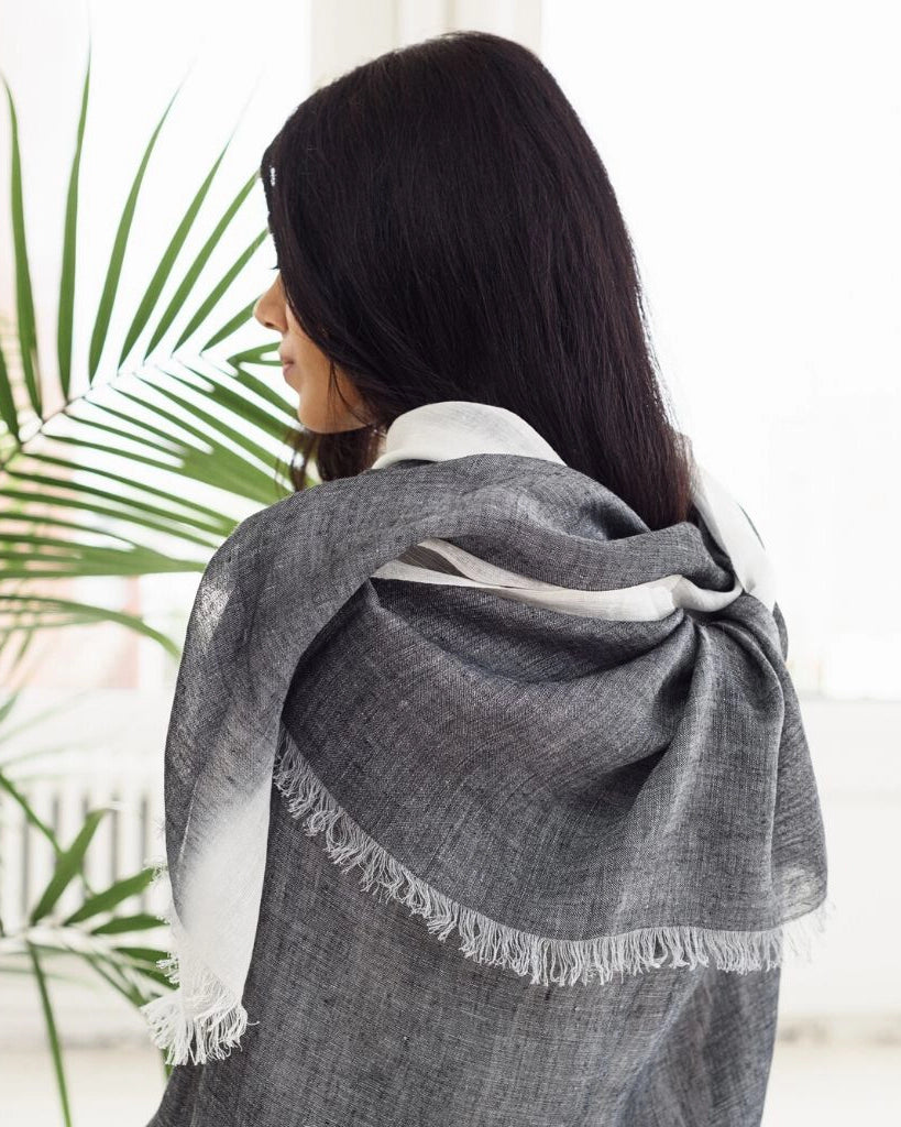 En handvävd linnehalsduk i grå och vit med fransar.