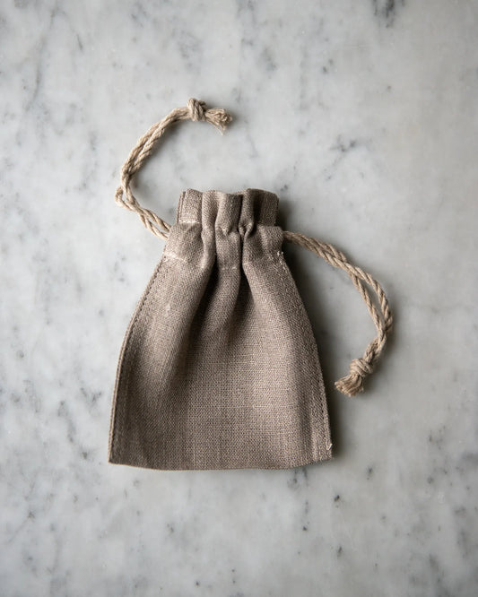 En liten handsydd linnepåse med dragsnöre ligger på en marmorskiva.