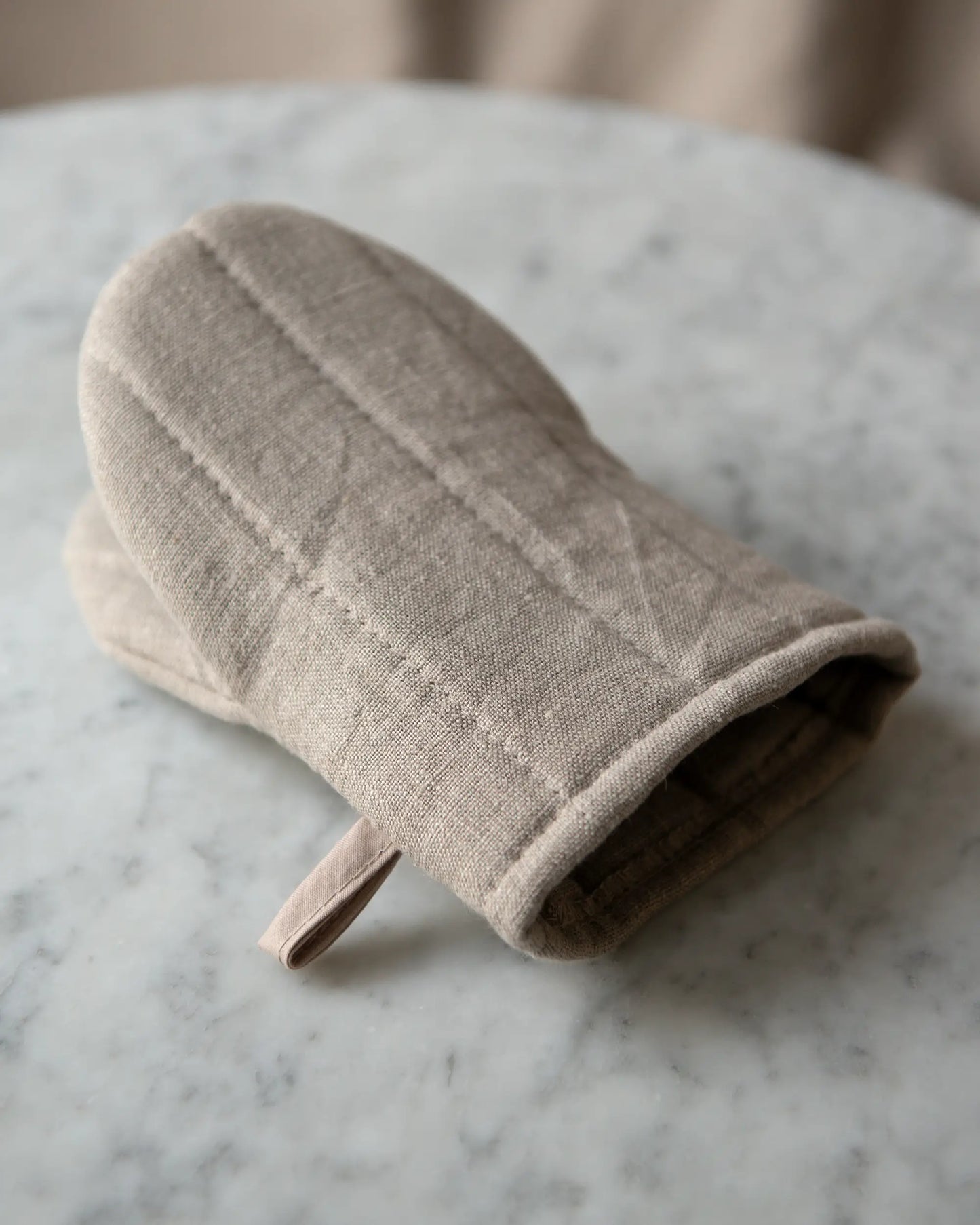 En handsydd grytvante i beige med ögla för upphängning.