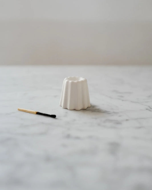 En liten handgjord ljusstake i vit keramik står på en marmorskiva med en tändsticka som ligger bredvid. 