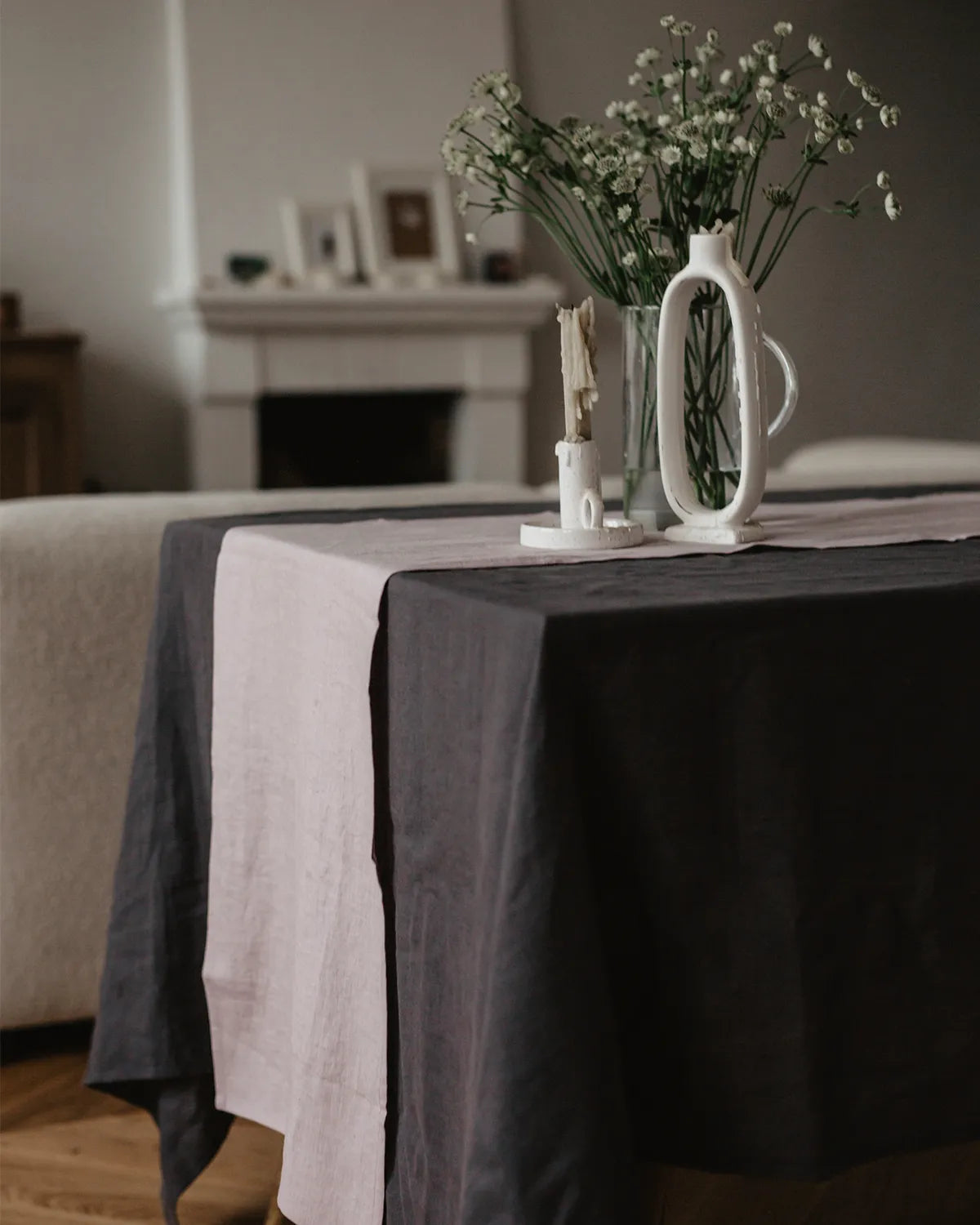 En mörkgrå linneduk ligger på ett bord och på bordet står en glasvas och ljusstake.  