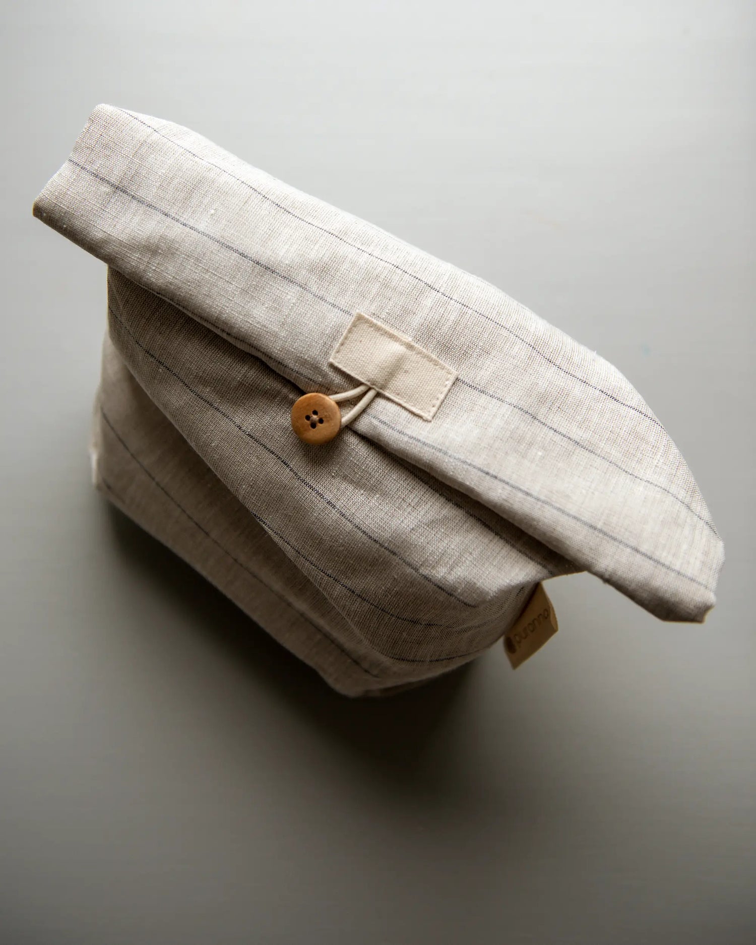 En randig handsydd lunchpåse i linne med en brun knapp som står upp på en plan yta. 