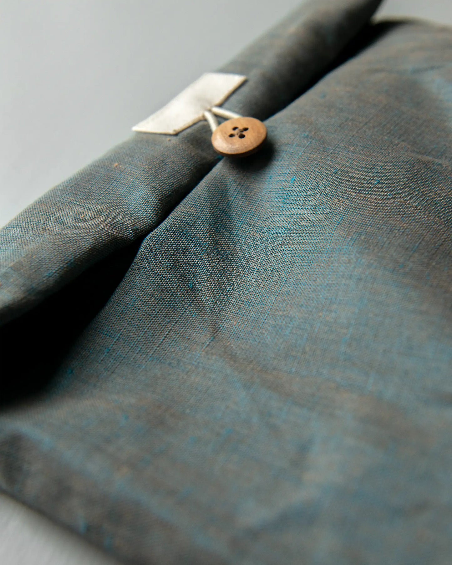 En grönmelerad handsydd luchväska i linne med en brun knapp. 