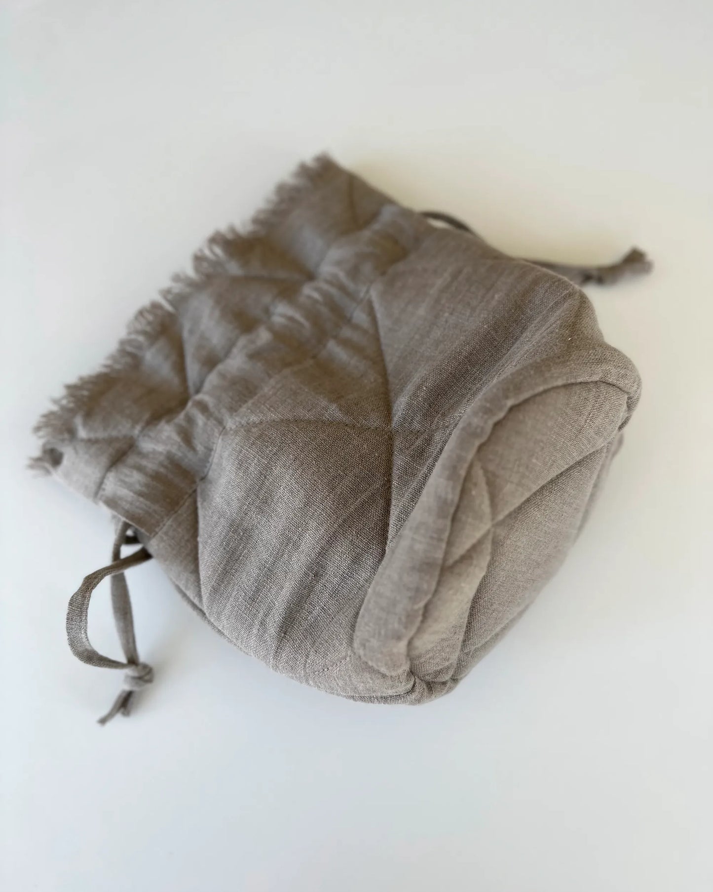 En handsydd vadderad och quiltad tygpåse med dragsko och vaddering i beige linnetyg.