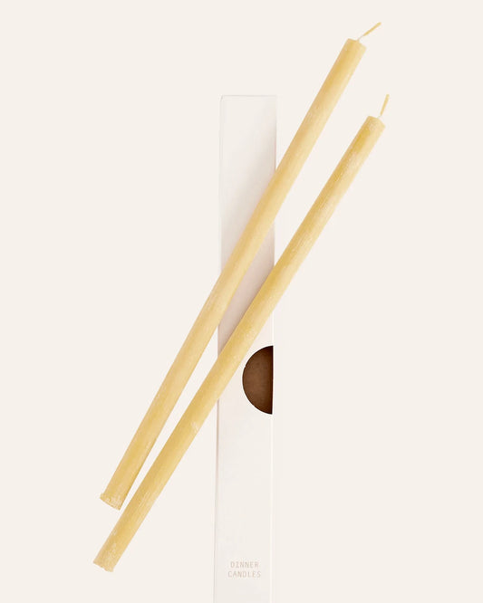 Två stycken handgjorda bivax ljus ligger bredvid varandra på sin vita pappersförpackning.