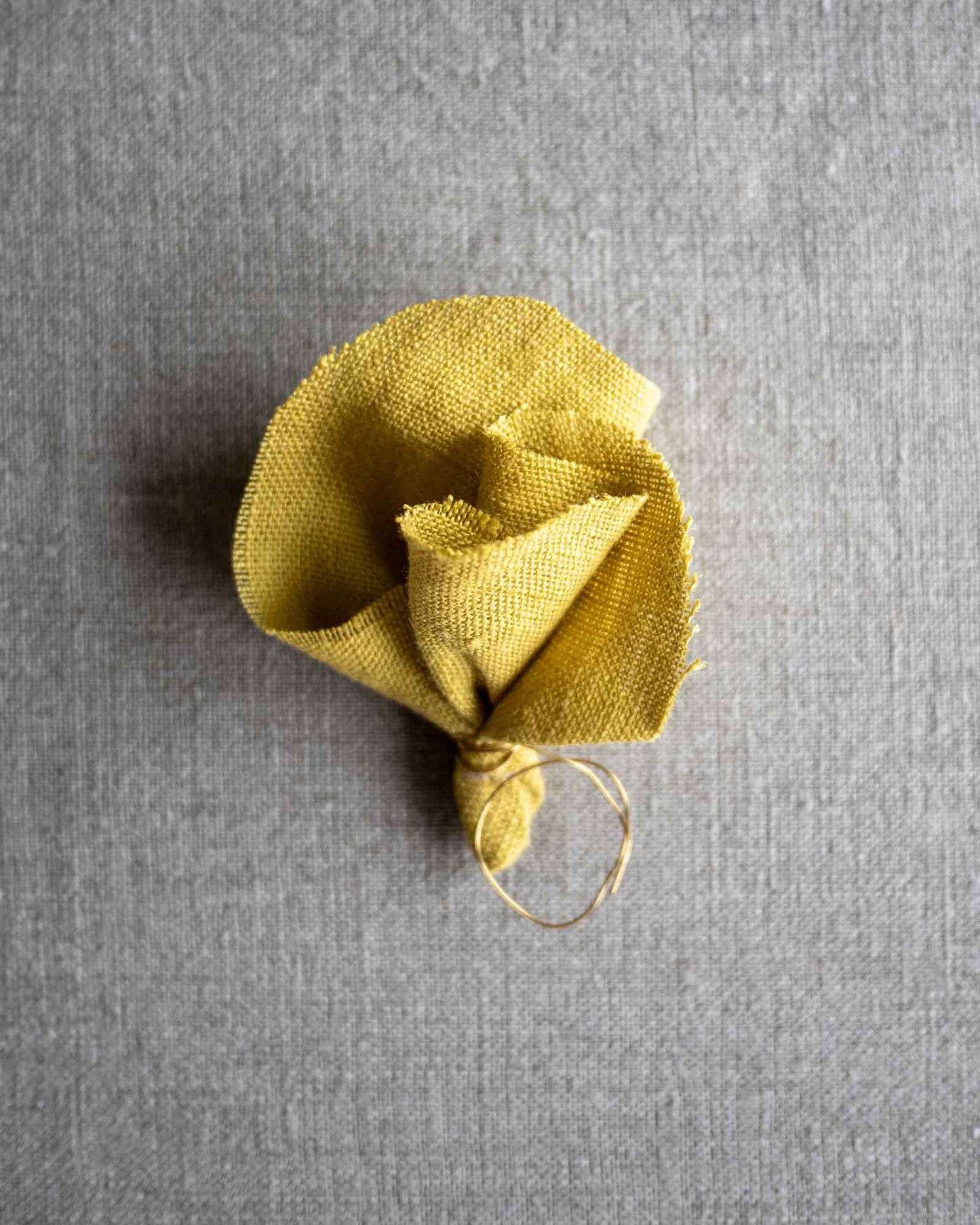 En liten handsydd tygblomma i gult linne ligger på en plan yta.