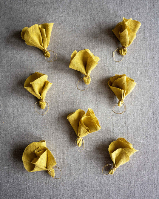 Åtta stycken gula tygblommor i linne ligger bredvid varandra på en grå plan yta.