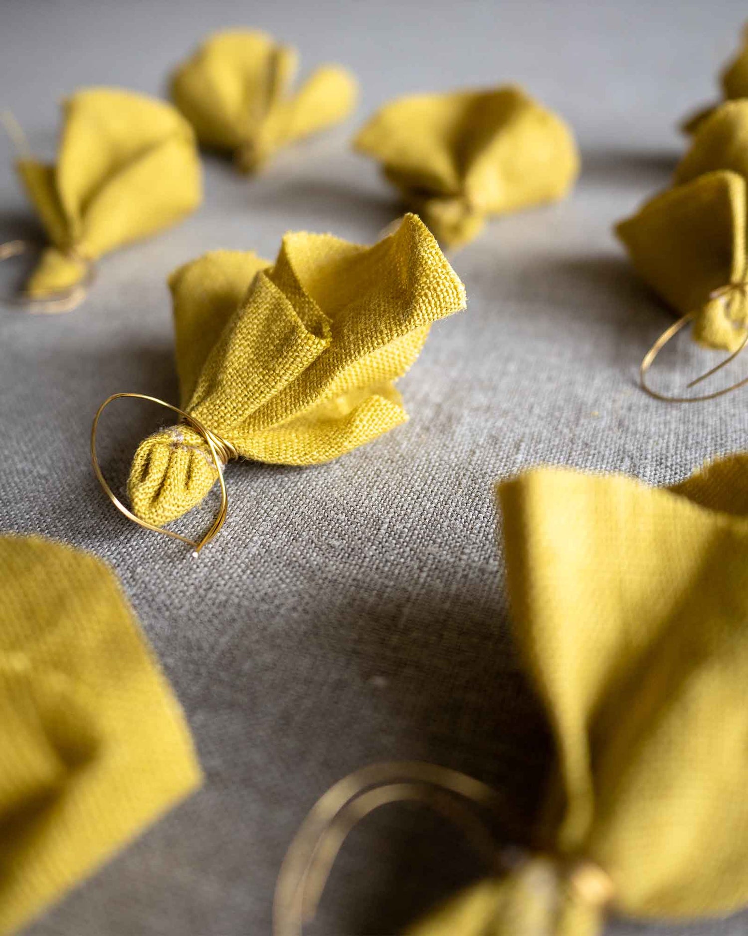 Åtta stycken handsydda tygblommor i gult linne med ståltråd ligger på en plan yta. 