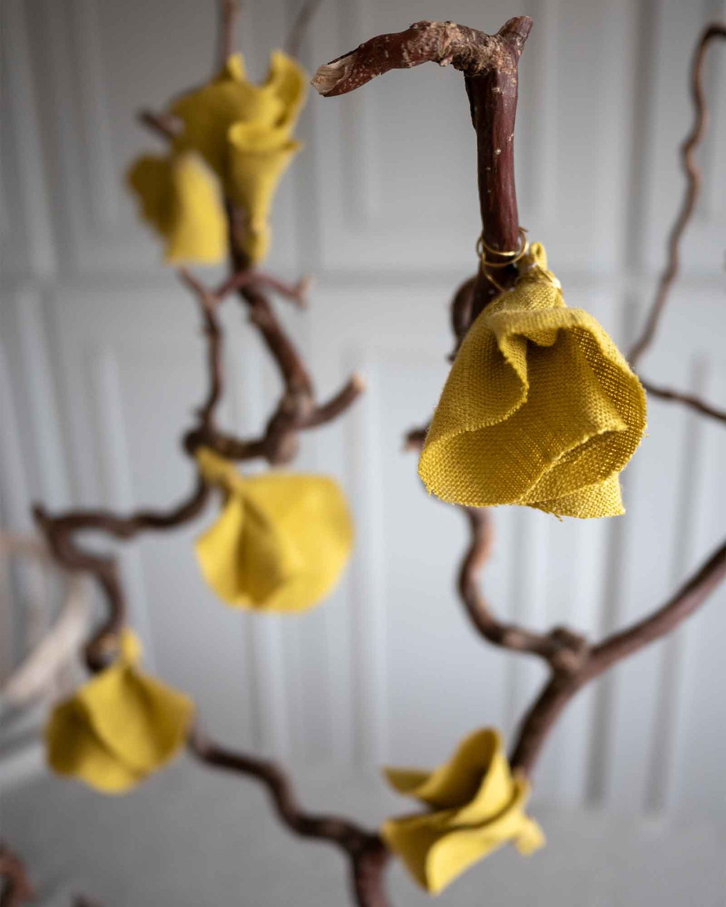 Sex stycken gula tygblommor i linne hänger på en gren. 