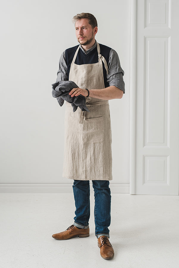 En kille bär ett köksförkläde i naturellt linne som sträcker sig ner till knäna.