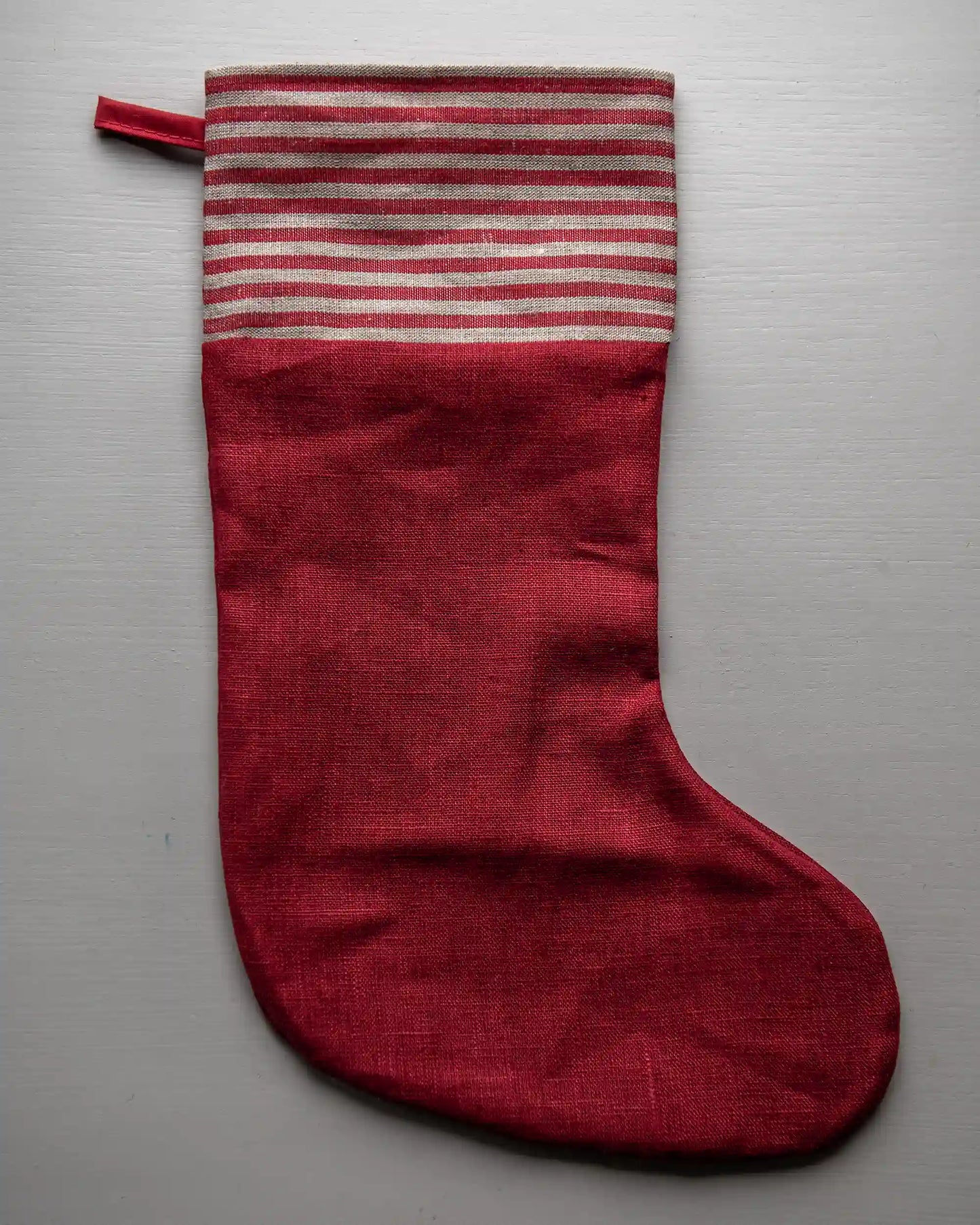 En handsydd röd julstrumpa i linne med en randig kant och ögla. 