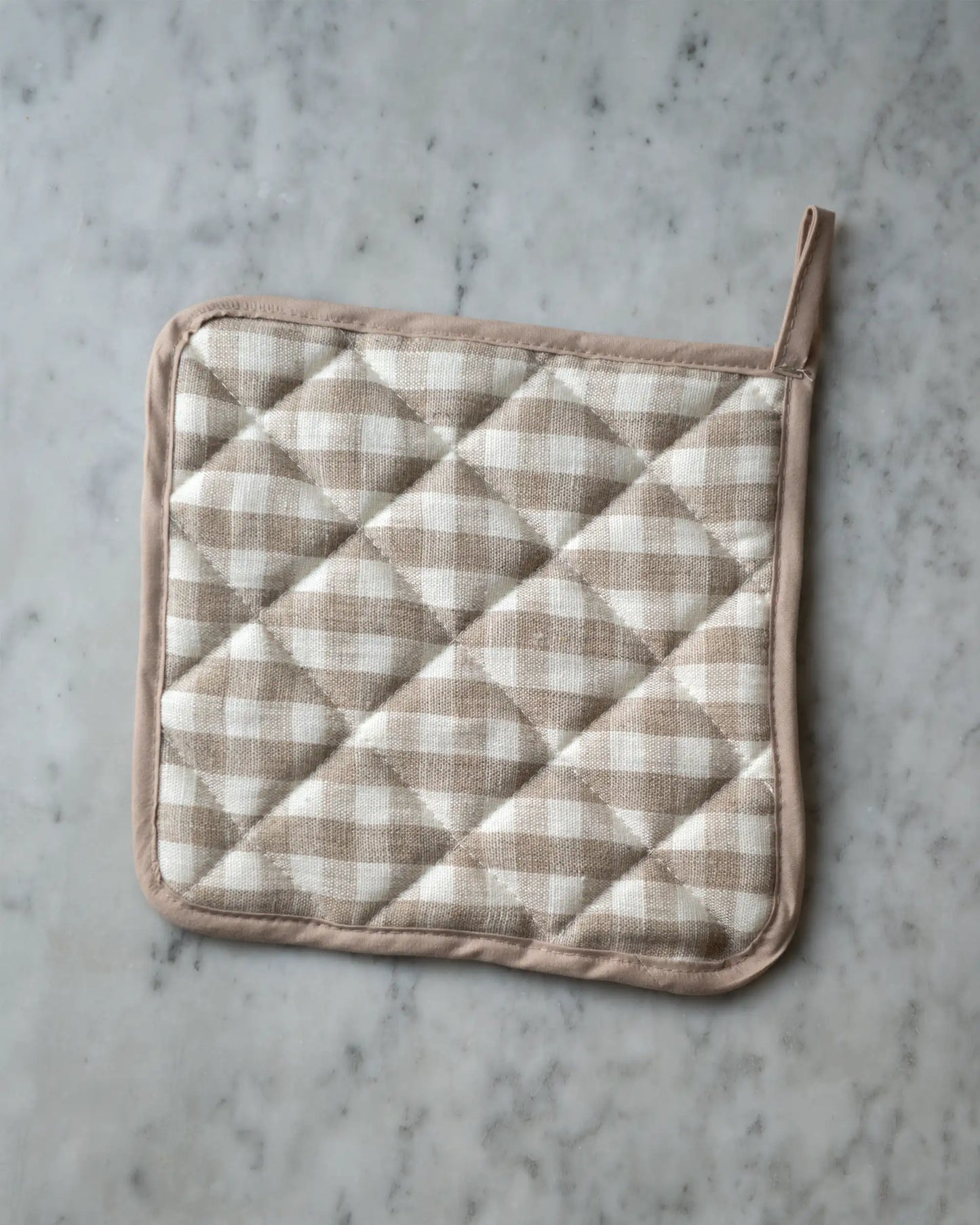 En handsydd rutig grytlapp i linne med beige och vita rutor.