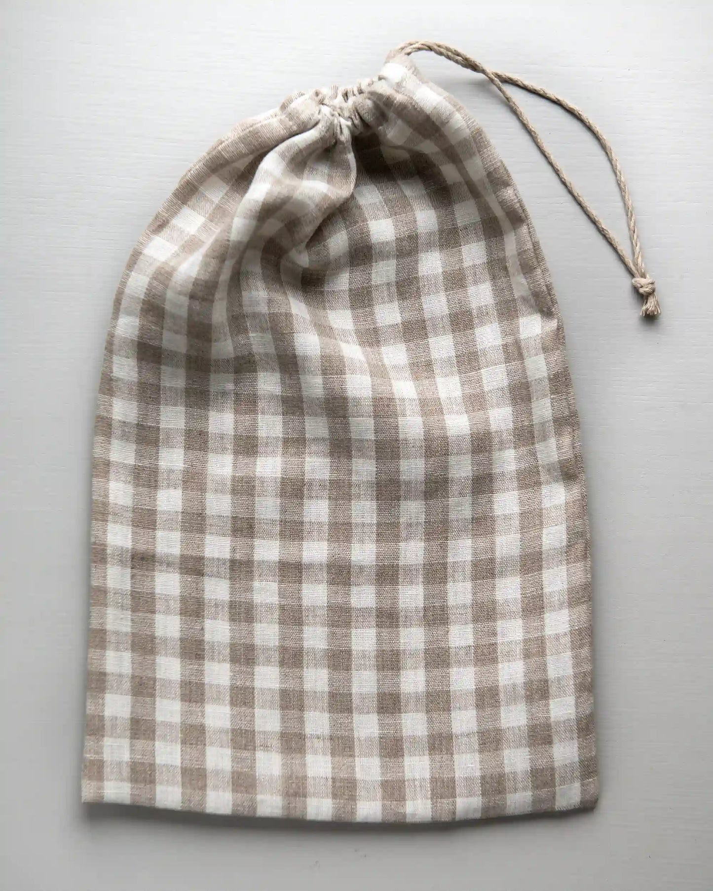 En handsydd brödpåse i rutigt linne som har dragits ihop med ett tunt band. 