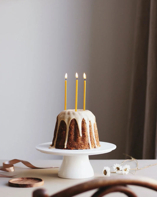 Tre stycken handgjorde smala bivax ljus står tända i en tårta.