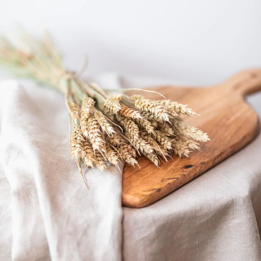 En bukett av torkat vete gräs ligger på en skärbräda tillsammans med en linneduk.