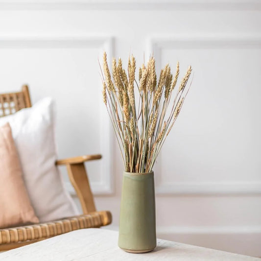 En bukett av torkat vete står i en grön vas på ett soffbord.