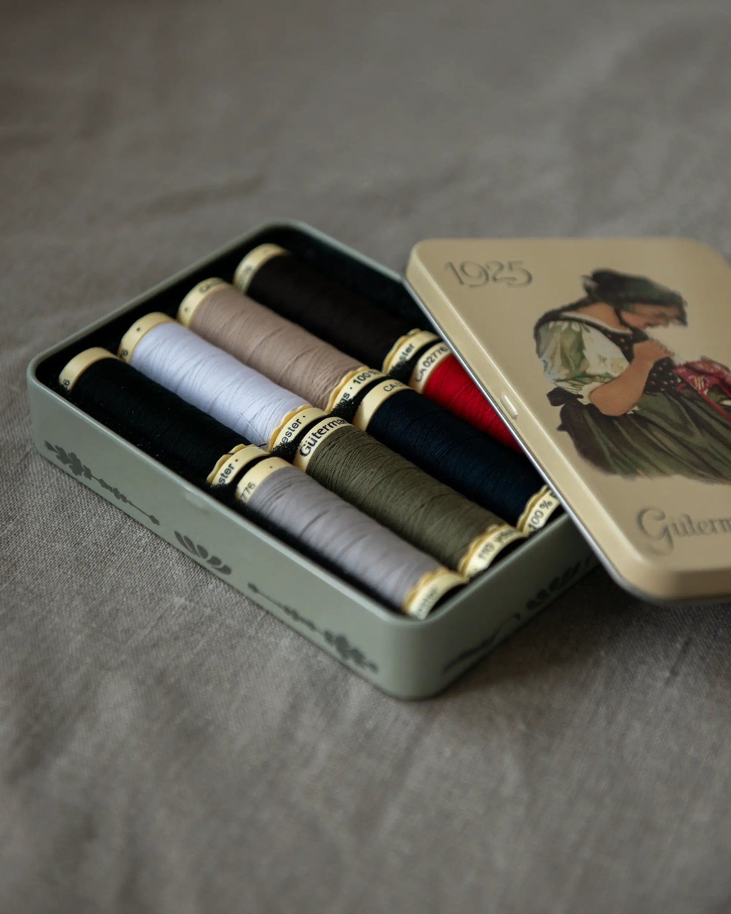Åtta stycken trådrullar i basfärger ligger i en vacker plåtask.