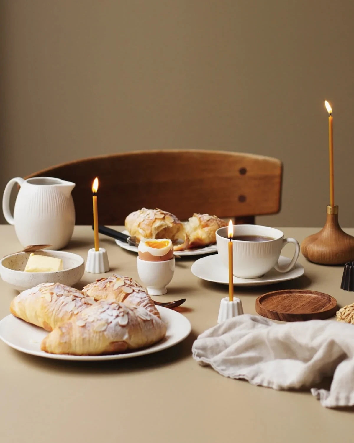 Ljushållare av oljad ek och keramik står på ett frukost bord med bivax ljus som är tända.