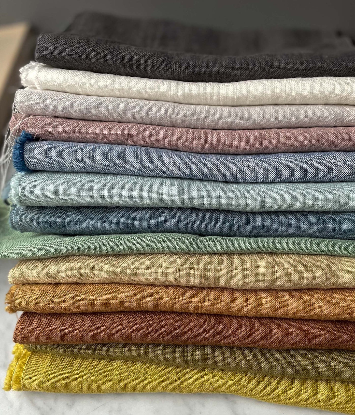 Olika färgskalor på ekologiskt linnetyg ligger ihopvikt i högar på varandra.