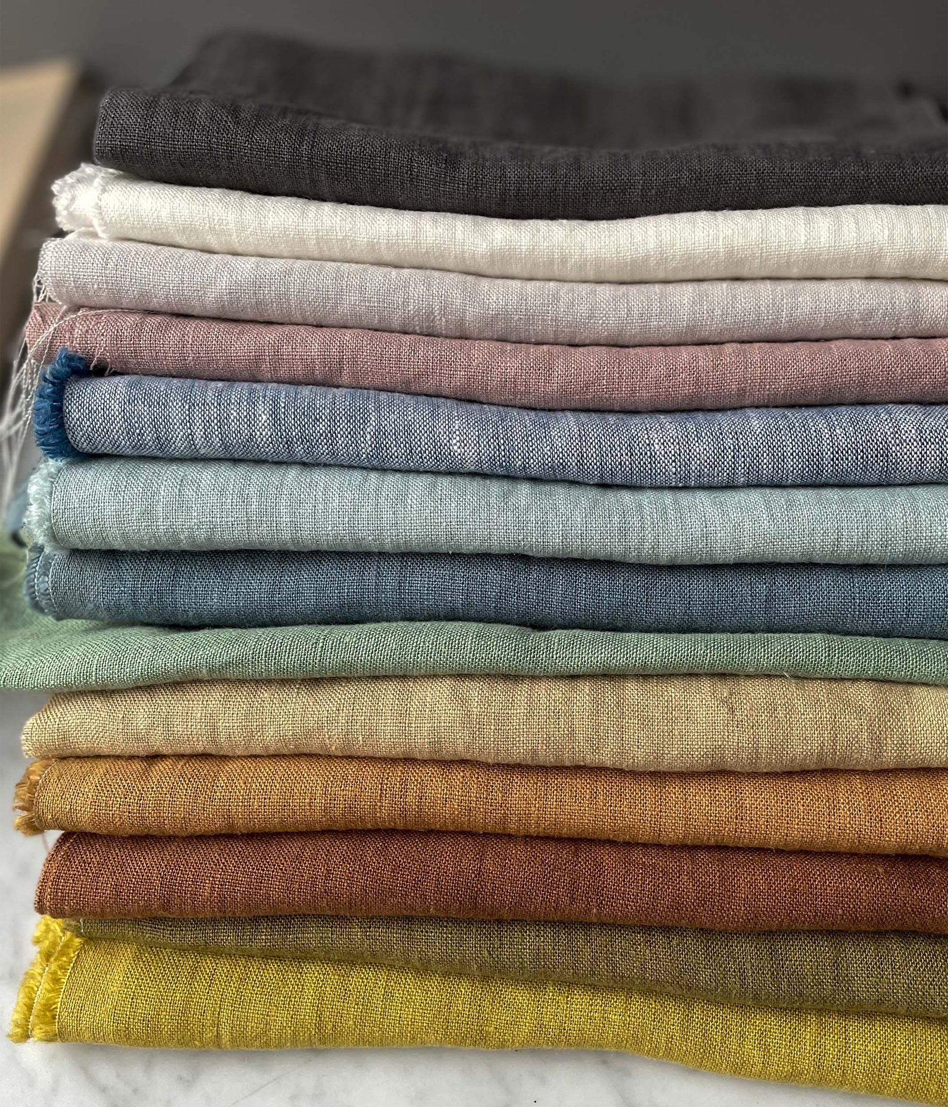 Olika färgskalor på ekologiskt linnetyg ligger ihopvikt i högar på varandra.