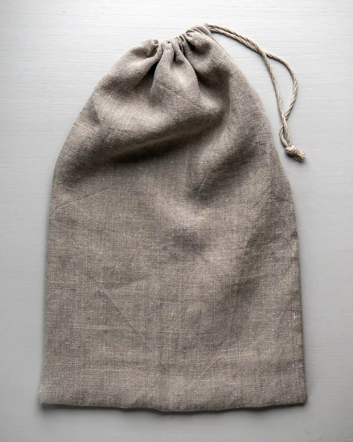 En handsydd brödpåse i naturell linne som har dragits ihop med ett tunt band.   