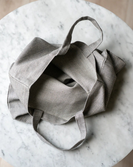 En handsydd grå tygpåse i 100% linne som ligger öppnad på ett marmorbord. 