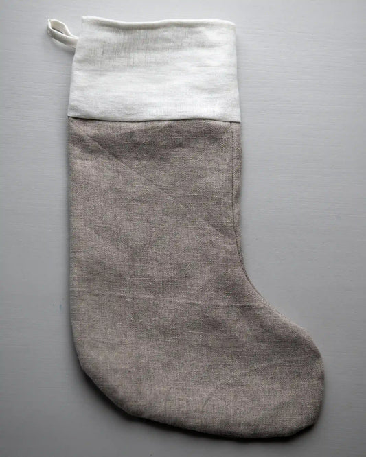 En julstrumpa i naturell linne med nedvikt kant i vit ligger på en plan yta.