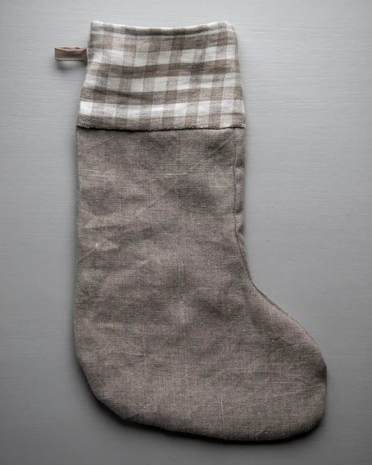En julstrumpa i naturell linne med en rutig kant och ögla.